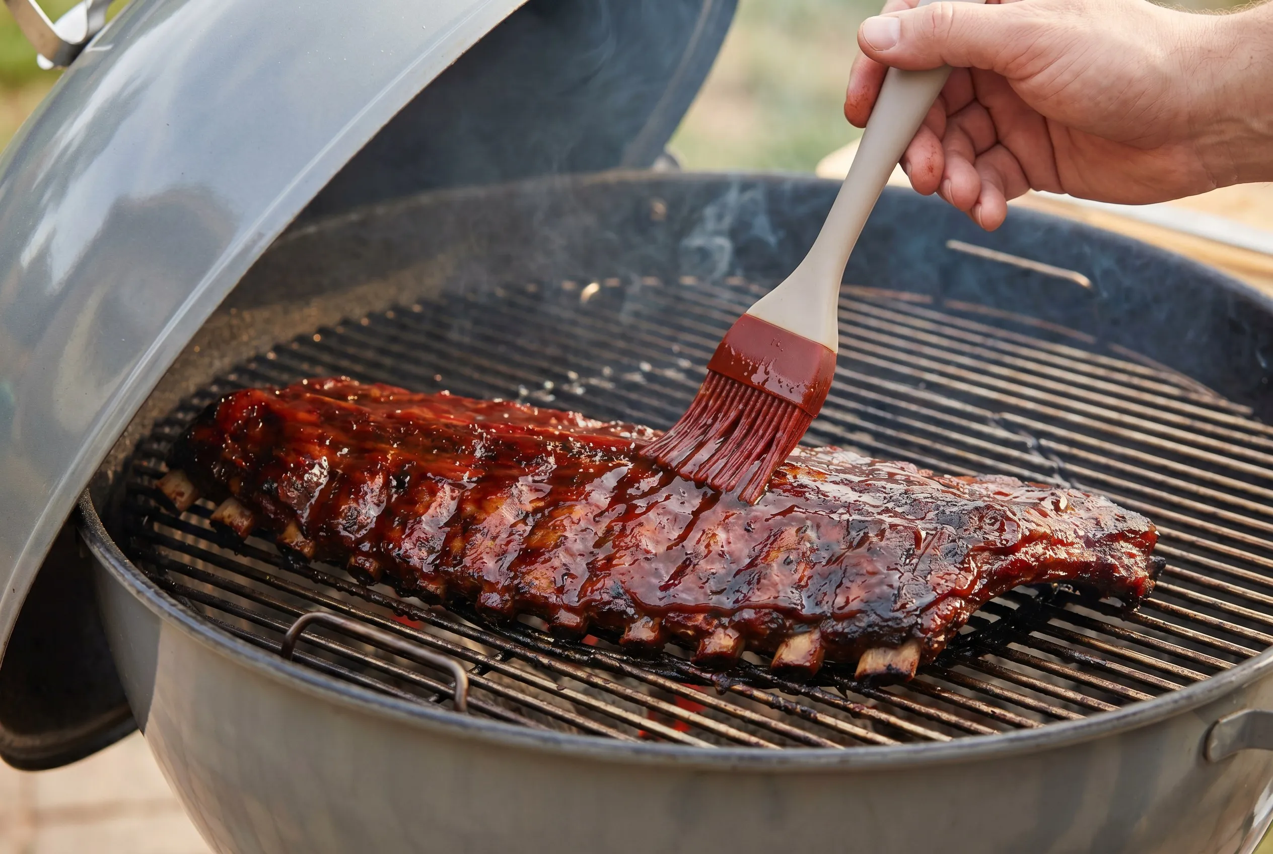 Spareribs på grillristen der pensles med rødbrun glaze af ketchup og honning
